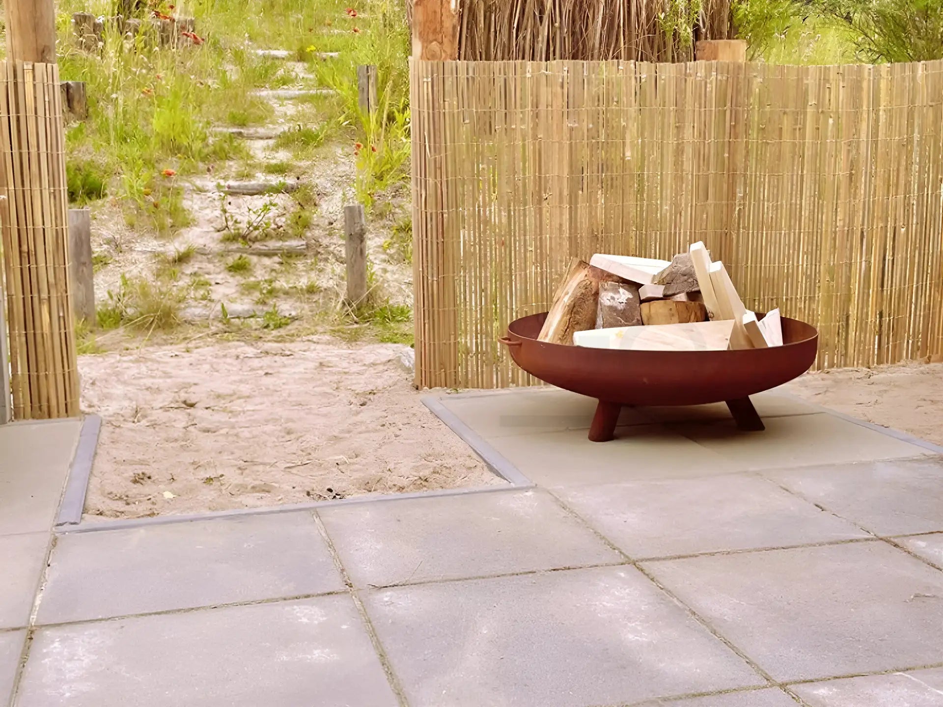 Lev vuurschaal van cortenstaal op een terras, klaar om aangestoken te worden, met natuurlijke tuin als achtergrond.
