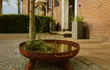 GoFire Lev waterschaal van cortenstaal met waterplanten, geplaatst op een terras naast een boom en grindstrook.