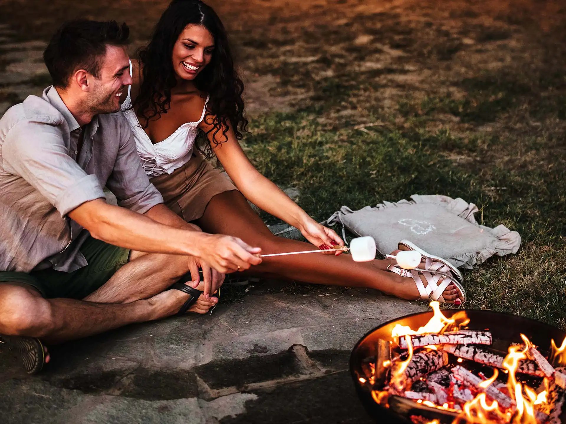 Een stel roostert marshmallows boven een brandende gofire oda vuurschaal, genietend van een gezellige en sfeervolle zomeravond buiten.
