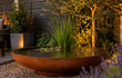 GoFire Oda waterschaal van cortenstaal als verlicht waterelement in de tuin bij avond, gevuld met water en waterplanten.