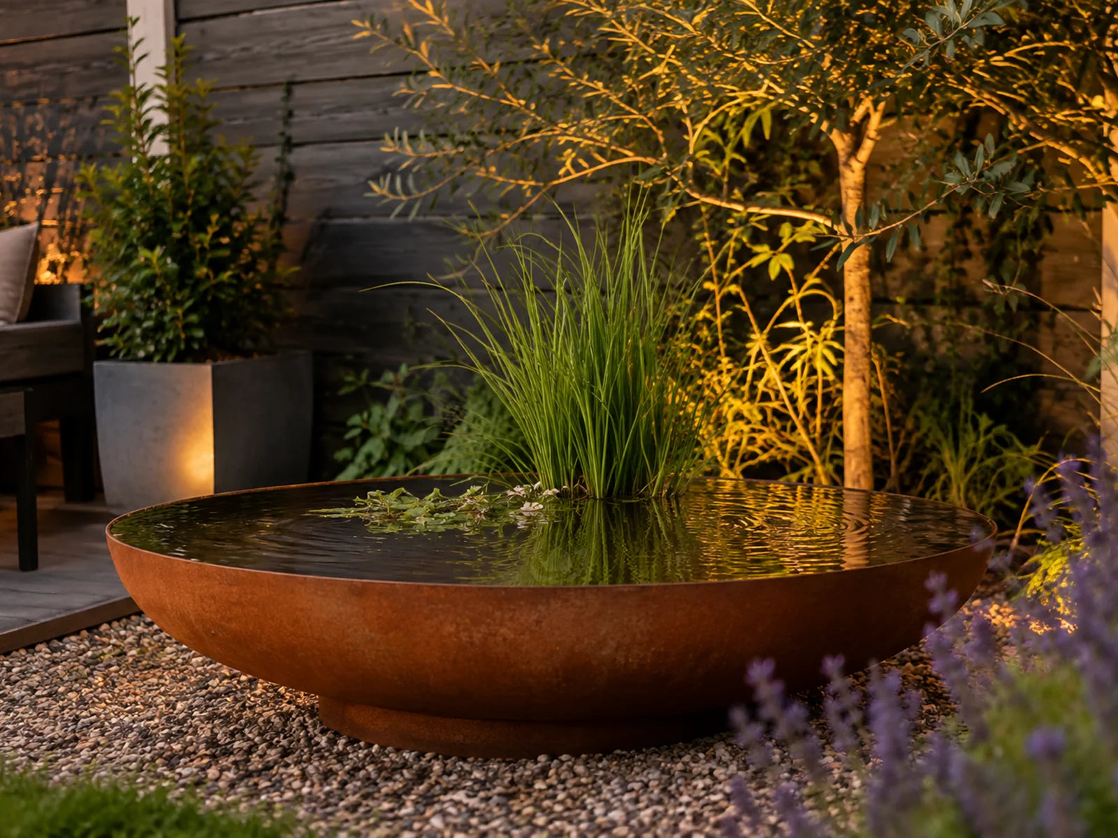GoFire Oda waterschaal van cortenstaal als verlicht waterelement in de tuin bij avond, gevuld met water en waterplanten.
