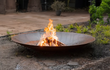 Gofire soho vuurschaal Cortenstalen met knisperend houtvuur, geplaatst in een tuinomgeving met groene planten en moderne bestrating.