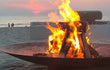 Gofire Soho vuurschaal van cortenstaal met brandend hout op het strand, terwijl de zon ondergaat en er een warme sfeer ontstaat bij de zee.
