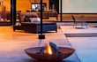 Gofire soho vuurschaal van cortenstaal met warm vuur, sfeervol geplaatst op een modern houten terras naast een luxe zithoek en grote ramen.