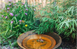 GoFire Soho waterschaal met fontein, omringd door bamboe en paarse bloemen, ideaal als stijlvol waterelement in de tuin.