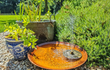 Gofire soho waterschaal met fontein geplaatst in een tuin tussen grind en groen, gevuld met water en sierplanten voor een natuurlijke uitstraling.