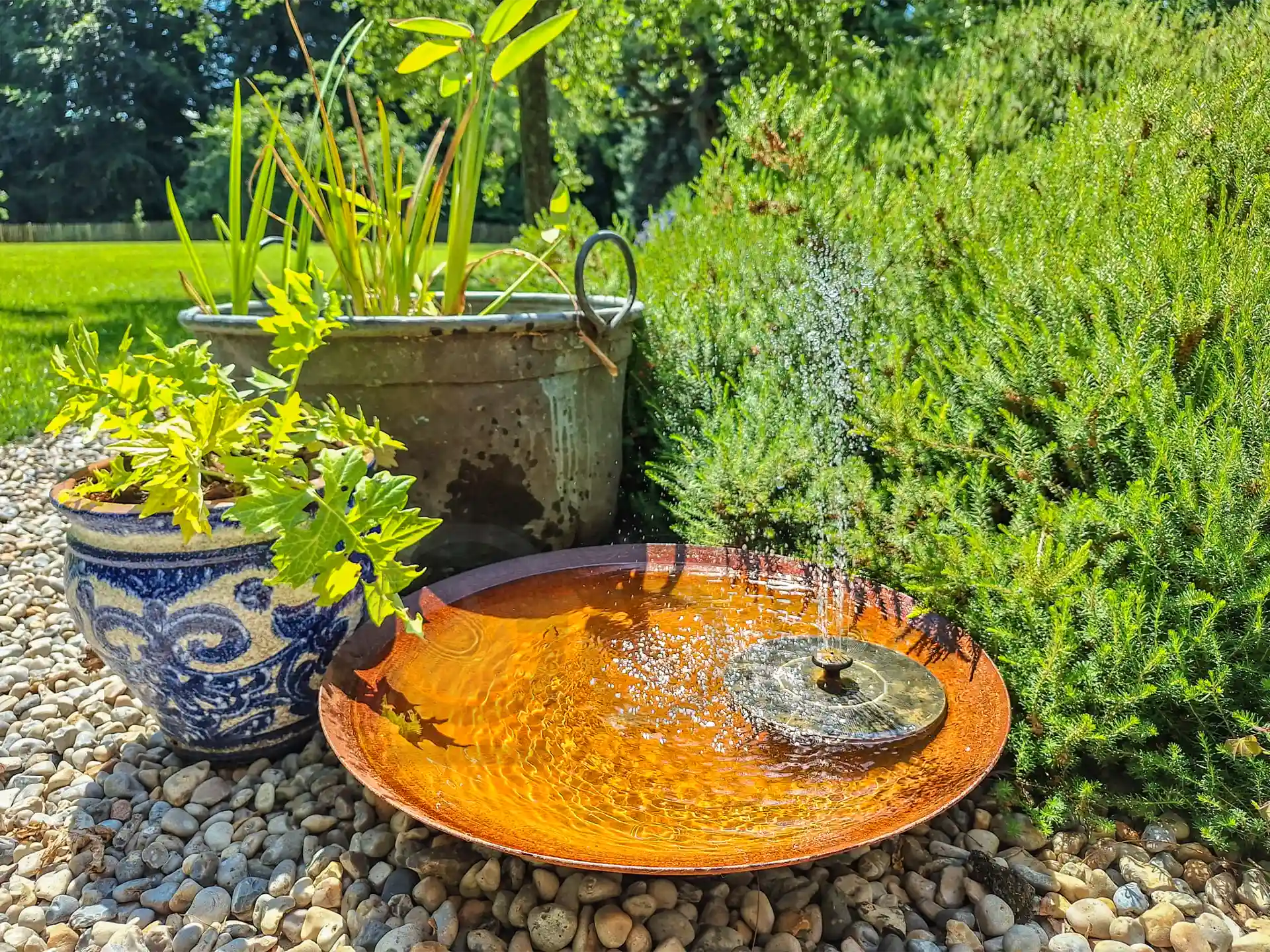 Gofire soho waterschaal met fontein geplaatst in een tuin tussen grind en groen, gevuld met water en sierplanten voor een natuurlijke uitstraling.
