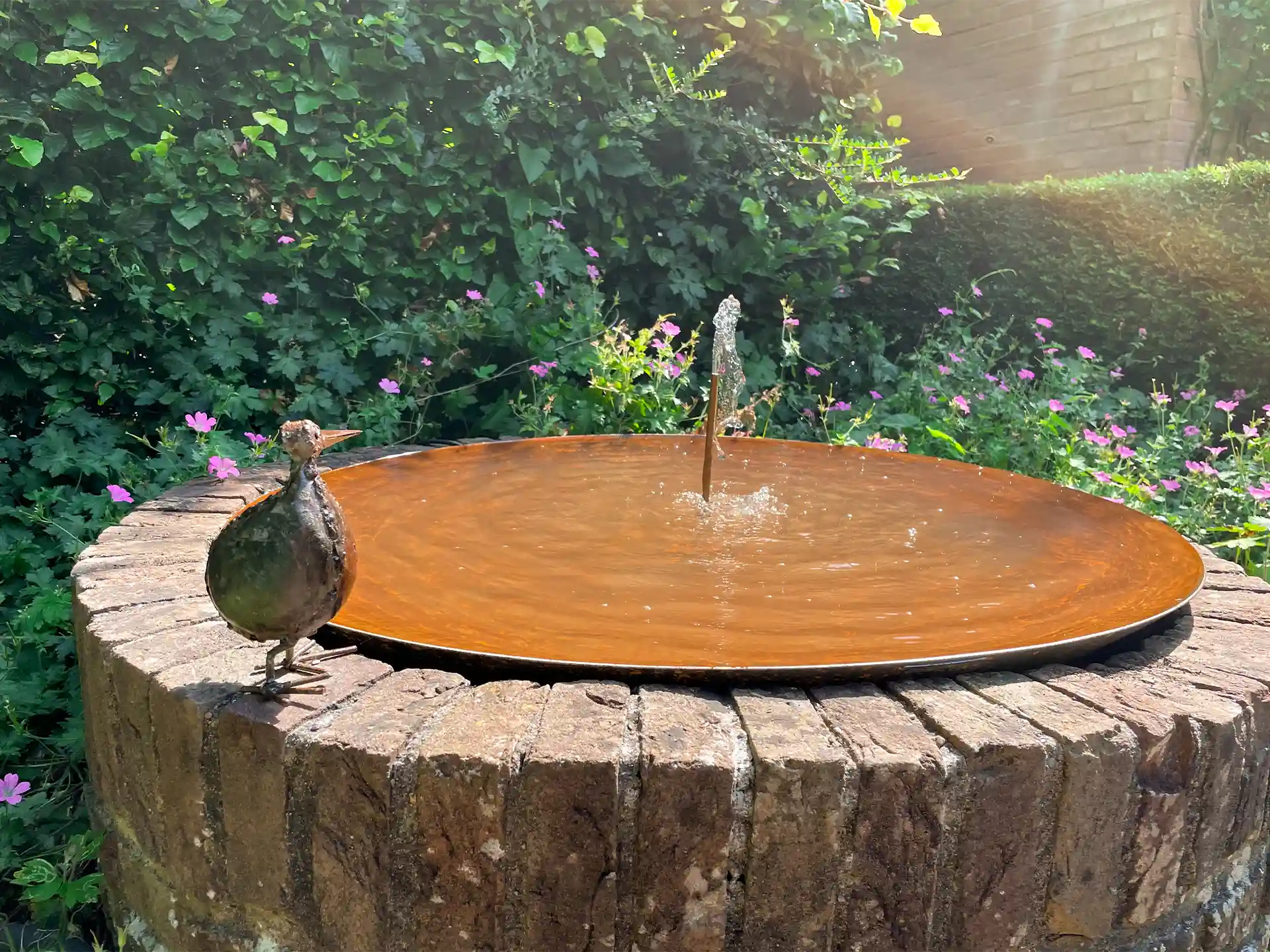 GoFire Soho waterschaal met kleine fontein, geplaatst op een boomstam met een vogel ernaast, ideaal als waterelement en vogelbad in de tuin.