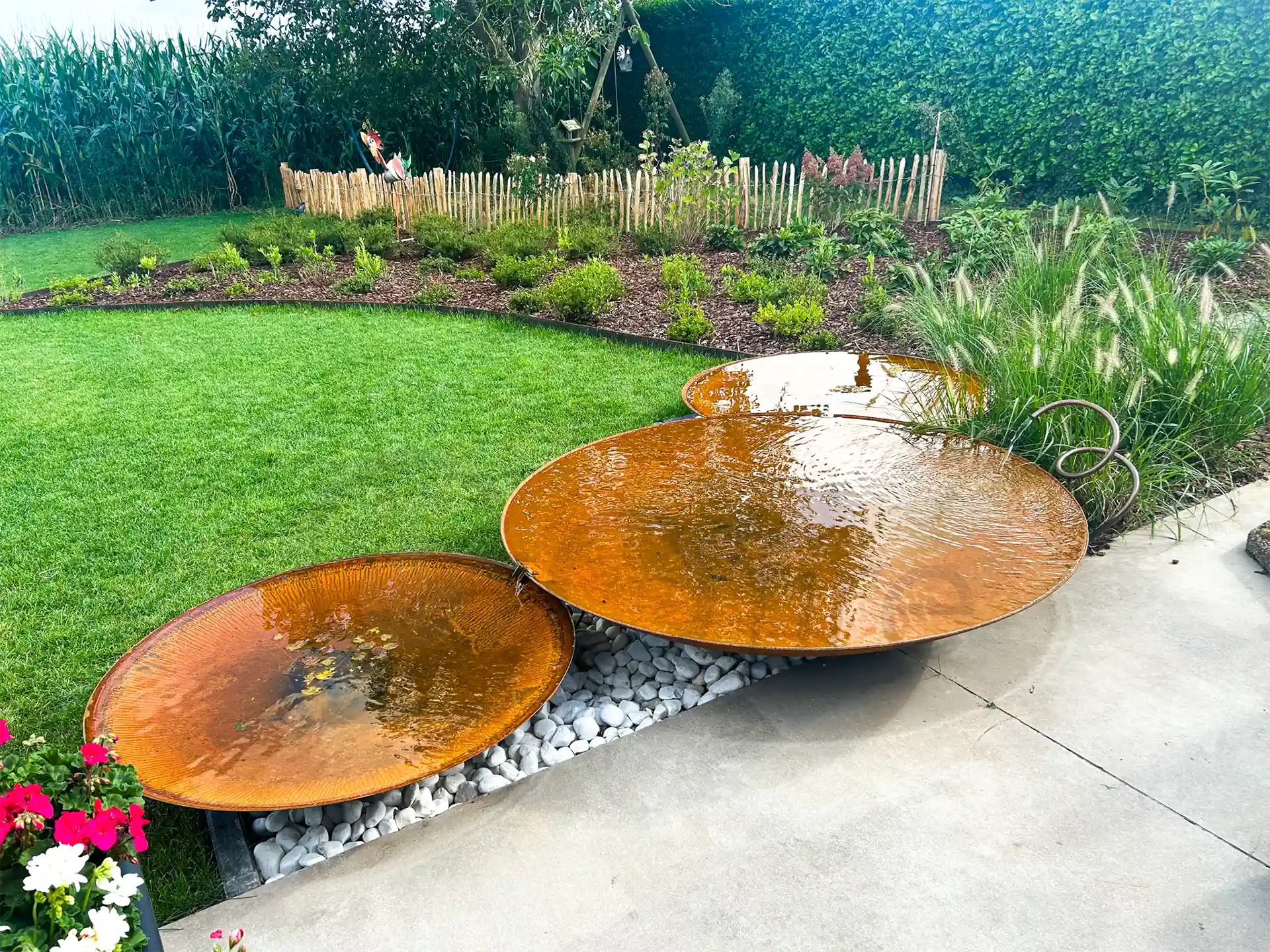 Set van GoFire Soho waterschalen van cortenstaal met fonteintjes, geplaatst naast elkaar in een moderne tuin met gazon en sierplanten.