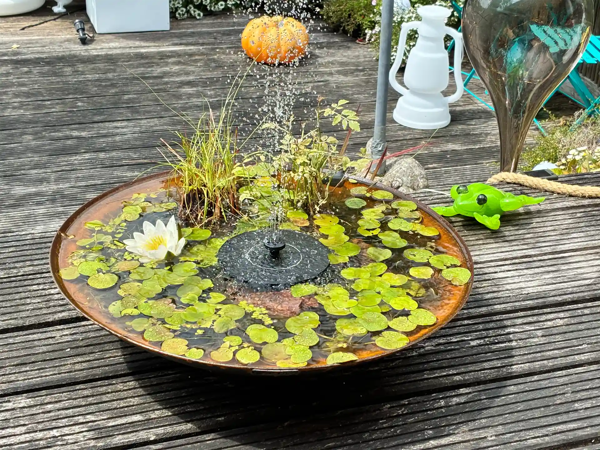 Gofire waterschaal met fontein, waterlelies en drijvende bladeren, geplaatst op een houten terras voor een sfeervol en rustgevend waterelement.
