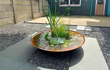 Gofire waterschaal gevuld met waterplanten en fontein, geplaatst op een modern terras met grind en tegels voor een decoratief waterelement.