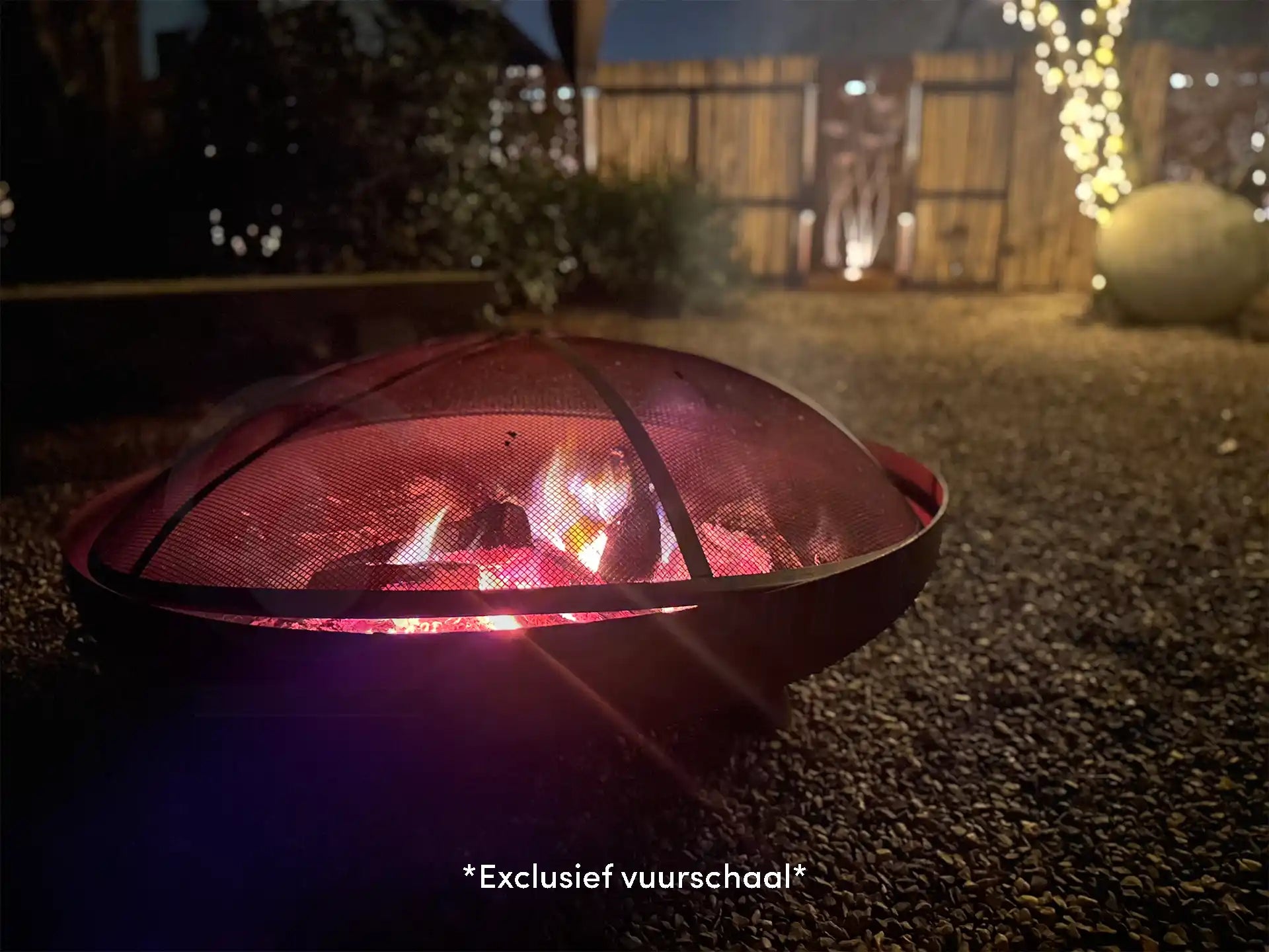 GoFire vonkenscherm voor vuurschaal in gebruik, geplaatst over een brandende vuurschaal in een sfeervolle tuin bij avond, met zichtbare vlammen achter het vonkenscherm.
