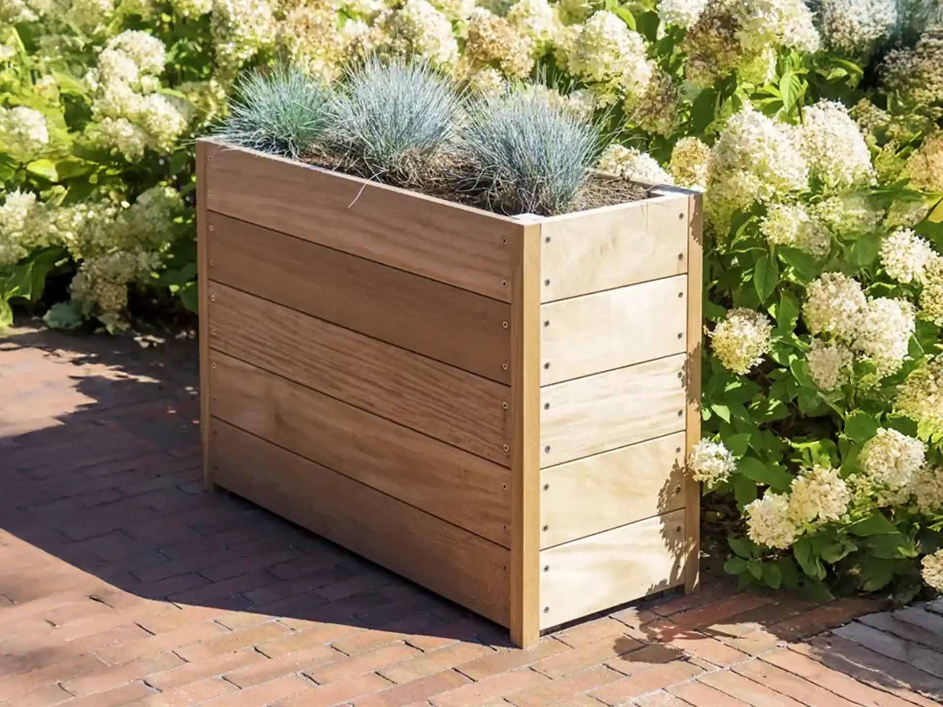 Adezz Carrez hardhouten plantenbak met bodem, beplant met siergrassen en vaste planten in een tuin.