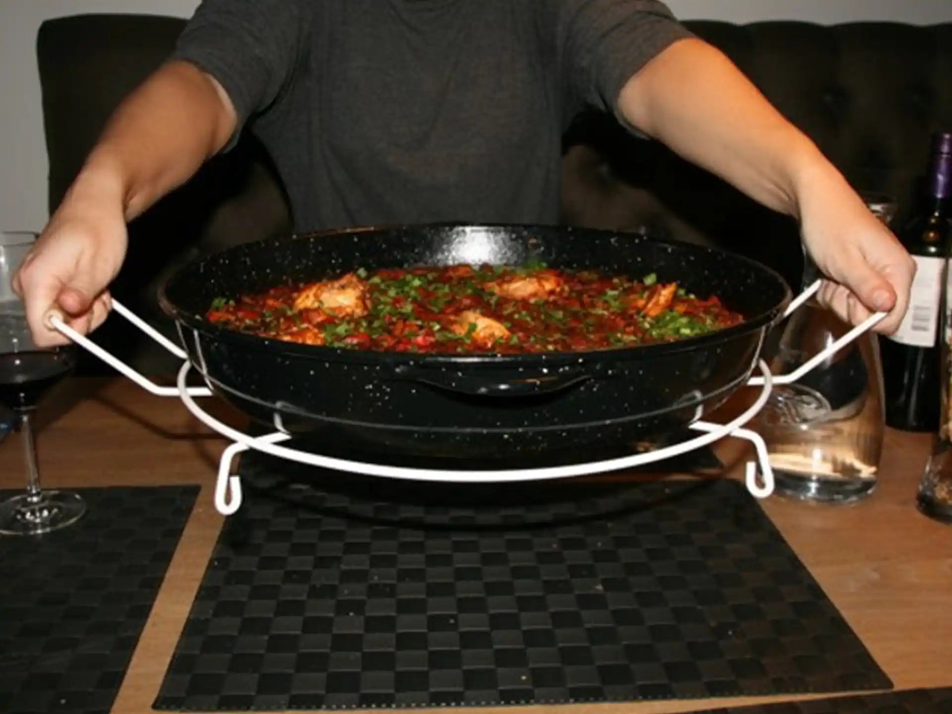 Onderzetter voor paella pan Deluxe in gebruik, persoon tilt pan vol paella van de tafel met stevige standaard.