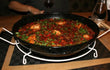 Paella pan gevuld met paella geplaatst op Deluxe onderzetter, stevige standaard op een houten tafel.