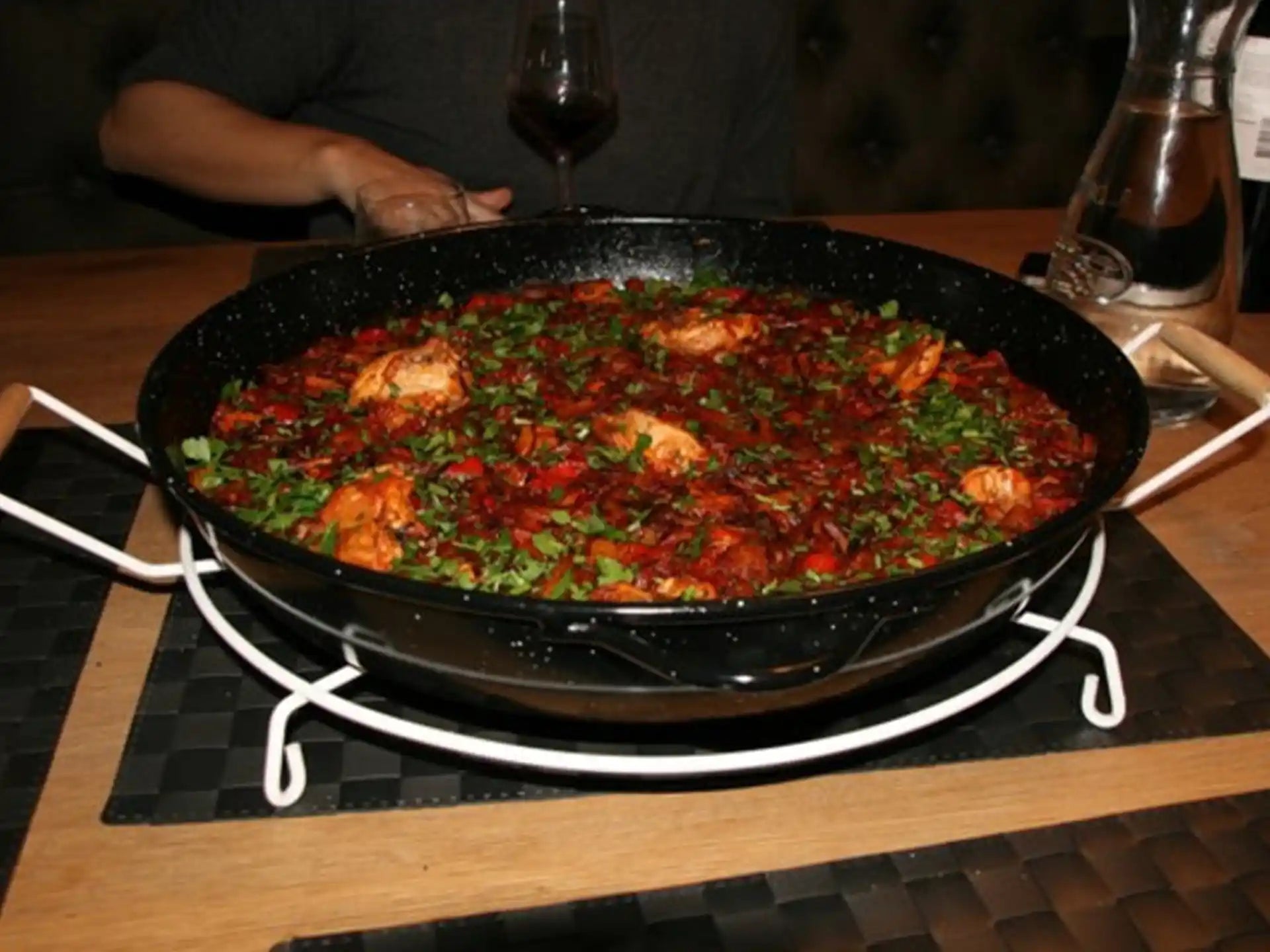 Paella pan gevuld met paella geplaatst op Deluxe onderzetter, stevige standaard op een houten tafel.