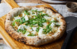 Vers gebakken pizza uit de Ooni Karu 12 pizza oven, geserveerd op houten plank met pizzaschep.