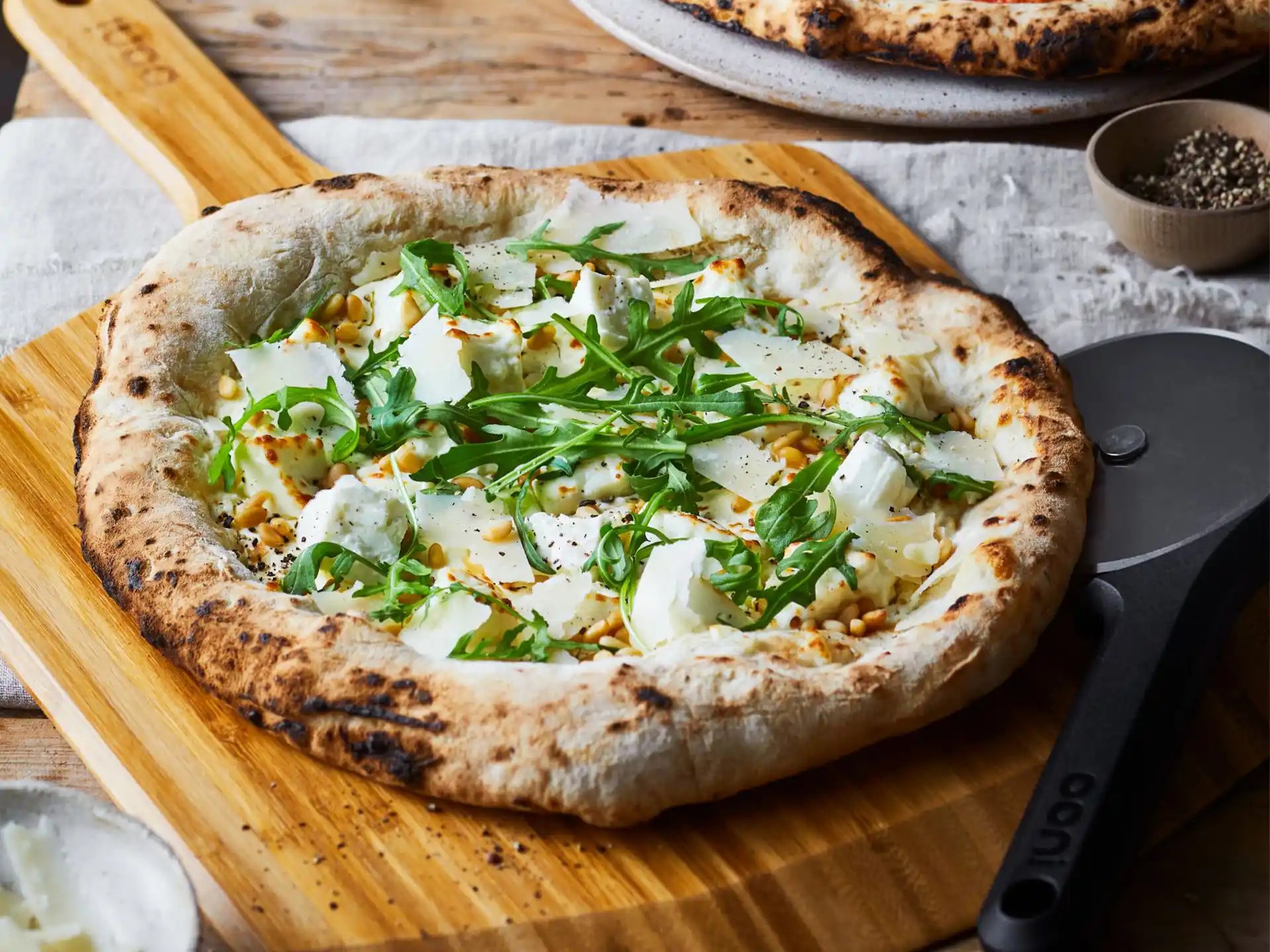 Vers gebakken pizza uit de Ooni Karu 12 pizza oven, geserveerd op houten plank met pizzaschep.