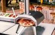 Ooni Karu 12 pizza oven in gebruik op tafel, hout- of houtskoolgestookte oven met pizza in de opening.