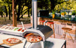 Ooni Karu 2 pizza oven hout of houtskool gestookt, in gebruik buiten met meerdere pizza’s op tafel.