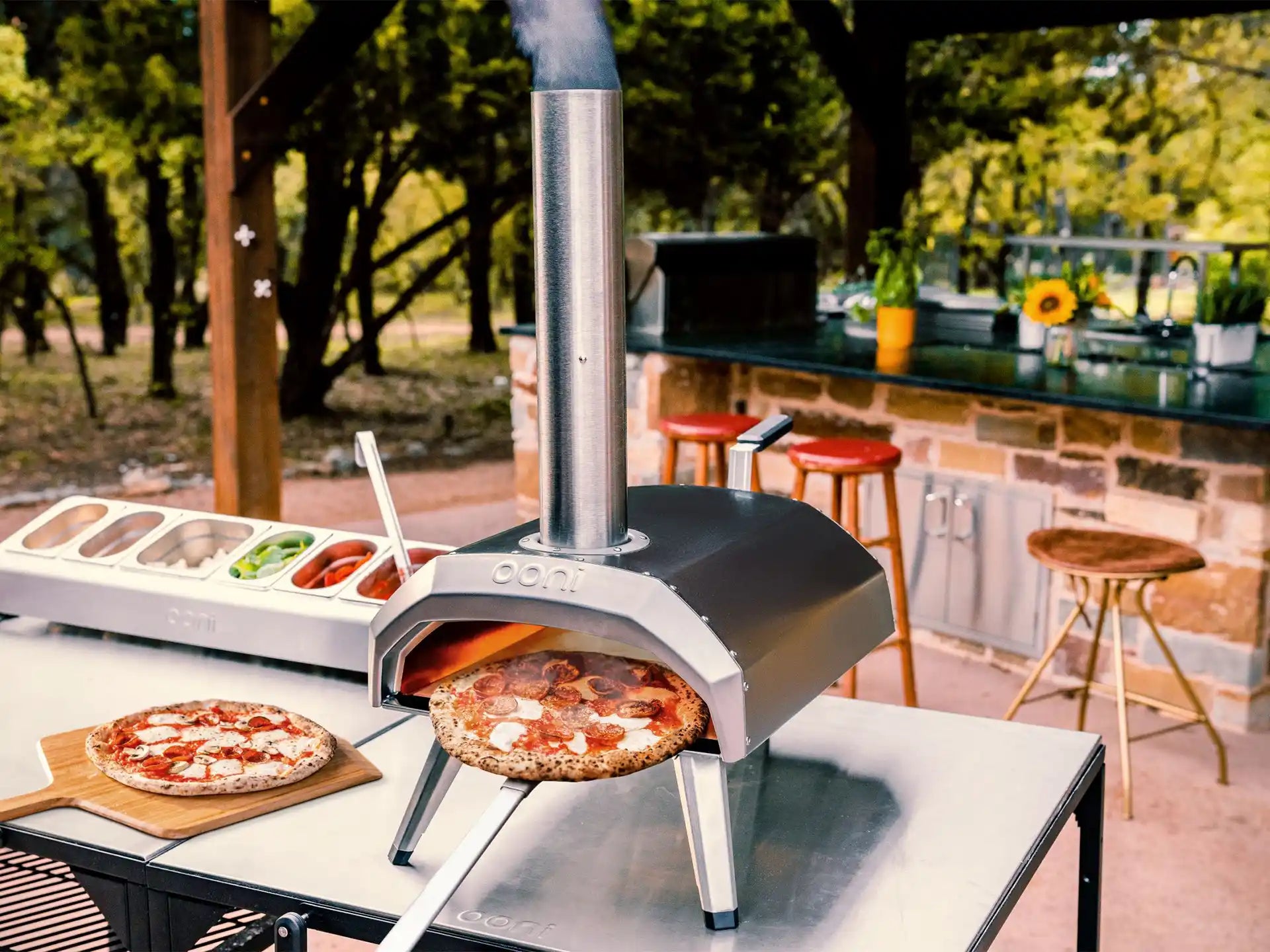 Ooni Karu 2 pizza oven hout of houtskool gestookt, in gebruik buiten met meerdere pizza’s op tafel.