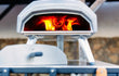 Close-up van Ooni Karu 2 hout- of houtskoolgestookte pizza oven, pizza bakt met zichtbare vlammen.