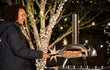 Ooni Karu 2 pizza oven hout of houtskool gestookt, sfeervolle lifestyle foto van persoon die pizza bereidt buiten.