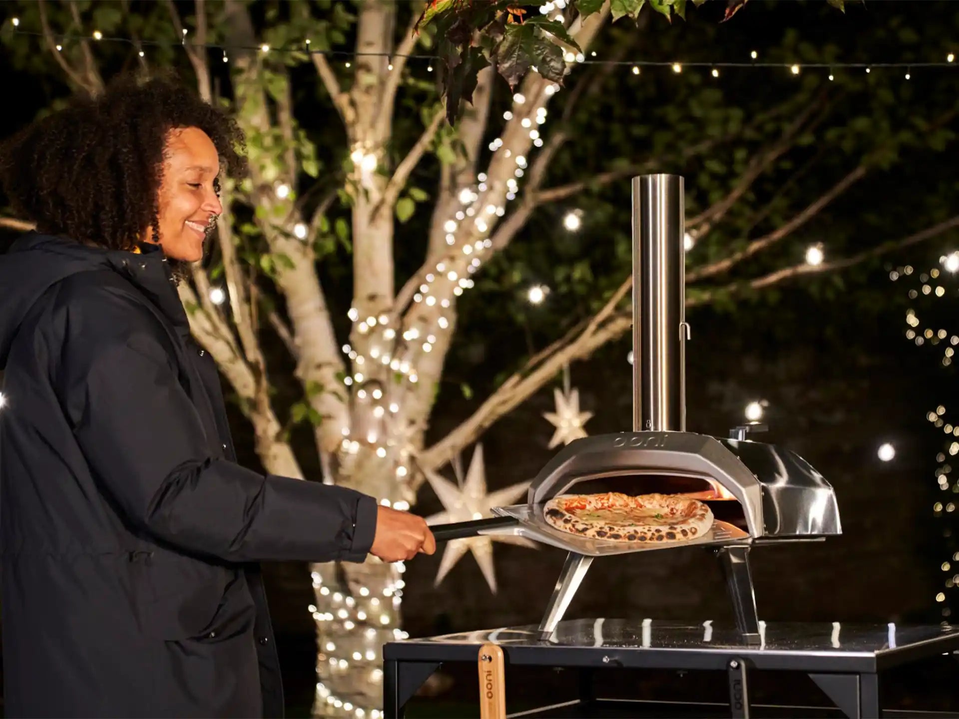 Ooni Karu 2 pizza oven hout of houtskool gestookt, sfeervolle lifestyle foto van persoon die pizza bereidt buiten.