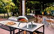 Ooni Karu 2 hout- of houtskoolgestookte pizza oven buiten op tafel, pizza bakt in de oven, sfeervolle setting.