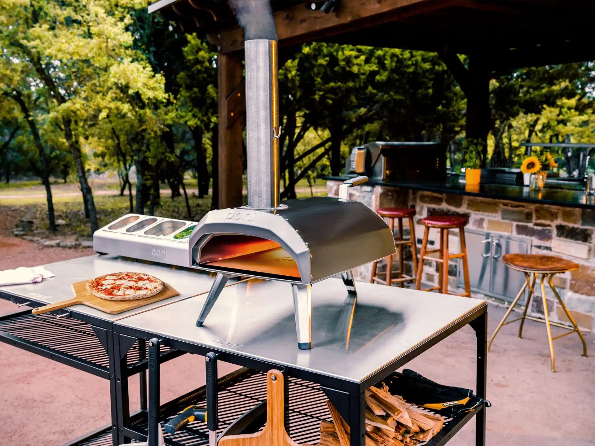 Ooni Karu 2 hout- of houtskoolgestookte pizza oven buiten op tafel, pizza bakt in de oven, sfeervolle setting.