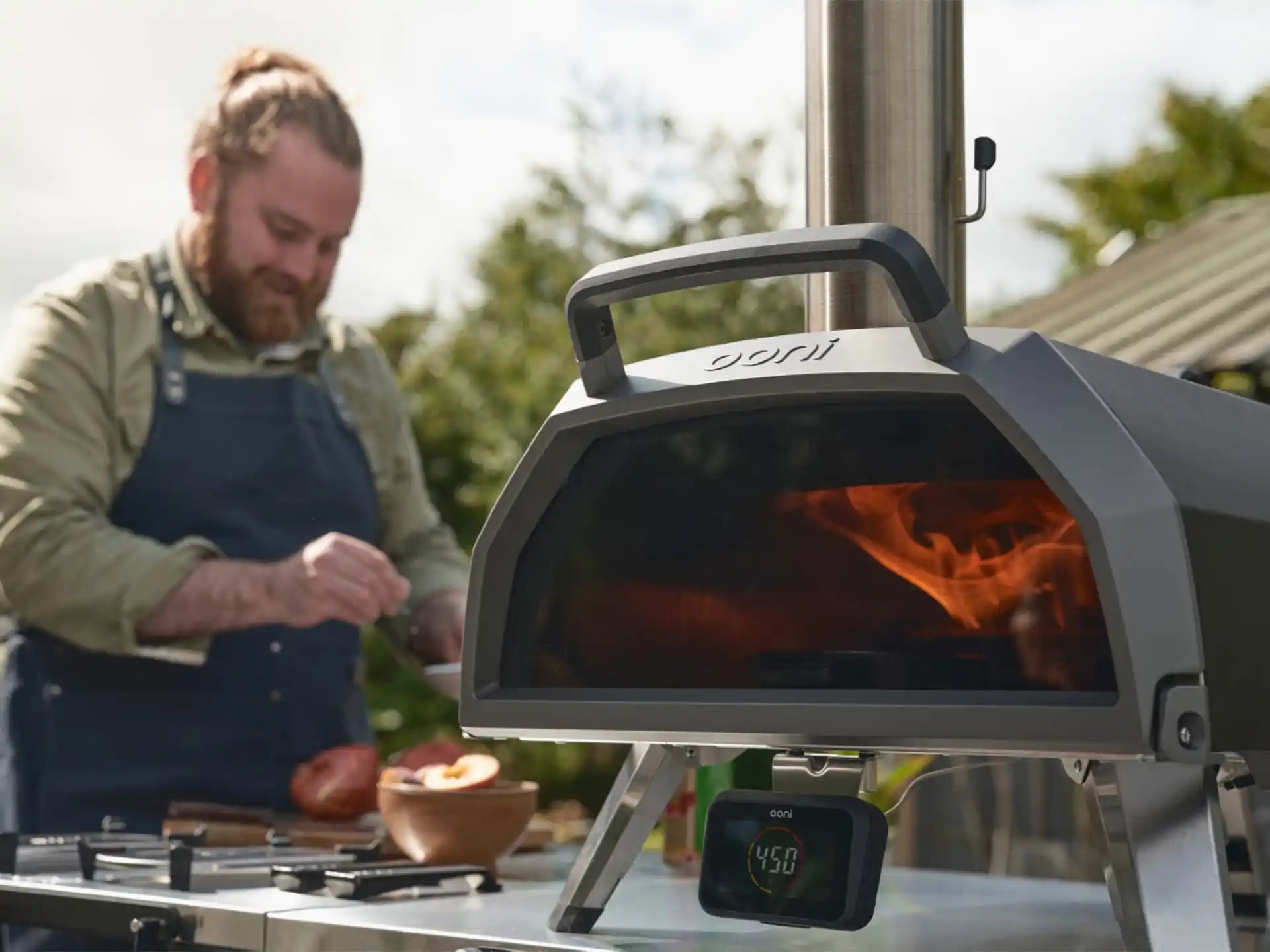 Ooni Karu 2 Pro hout- of houtskoolgestookte pizza oven in gebruik buiten, persoon bereidt pizza naast de oven.