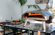 Ooni Koda 12 pizza oven op tafel buiten, pizza bakt in de gasgestookte oven, zomerse sfeer.