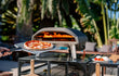 Ooni Koda 12 pizza oven buiten in een zonnige setting, pizza bakt in de gasgestookte oven op tafel.