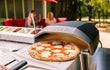 Ooni Koda 12 gas pizza oven buiten in gebruik, verse pizza op baksteen in de oven, sfeervolle setting.