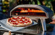 Ooni Koda 12 pizza oven buiten in gebruik, close-up van pizza die bakt in de oven.
