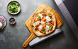 Vers gebakken pizza uit de Ooni Koda 16 pizza oven, geserveerd op houten plank met toppings.