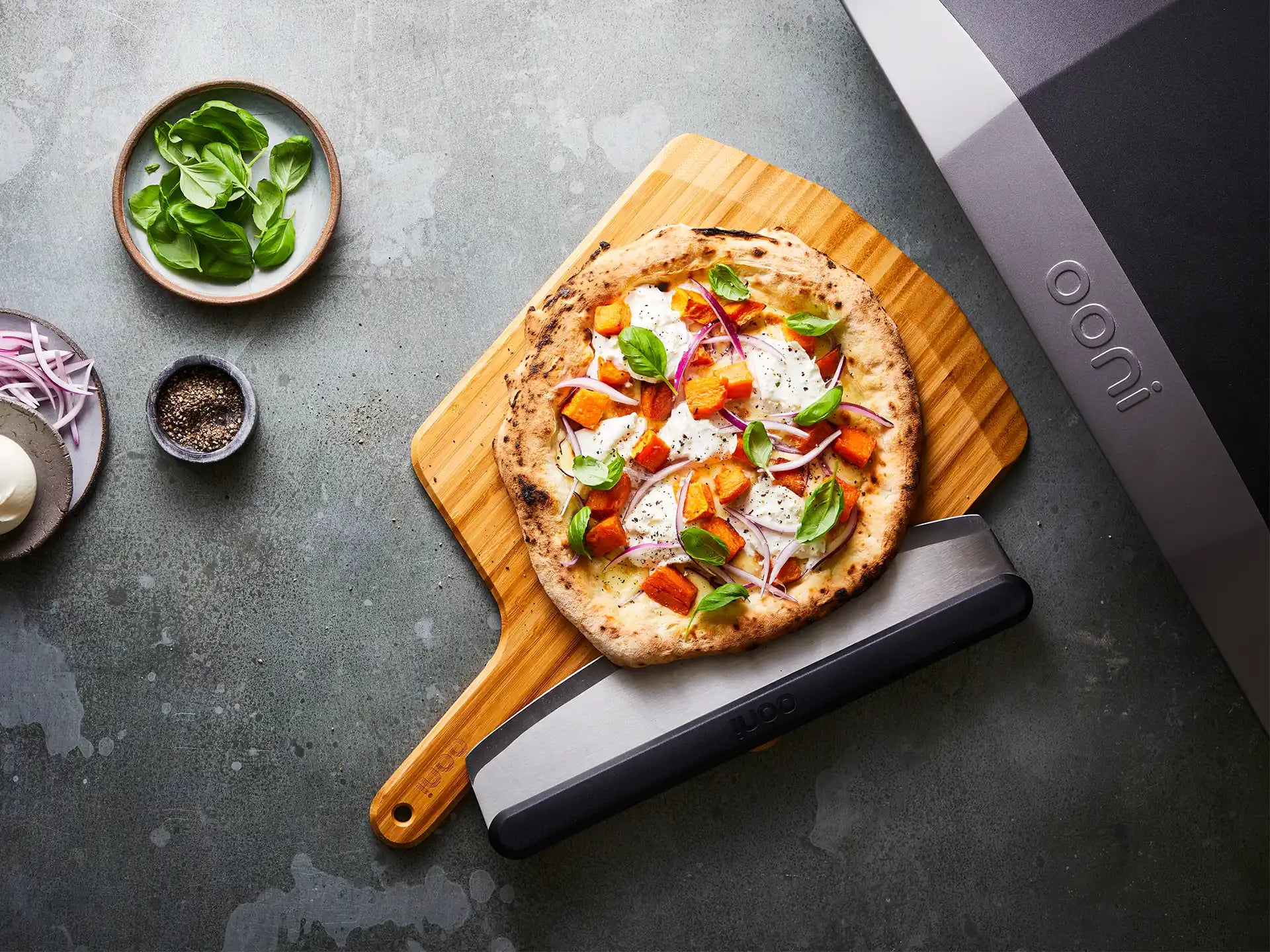Vers gebakken pizza uit de Ooni Koda 16 pizza oven, geserveerd op houten plank met toppings.