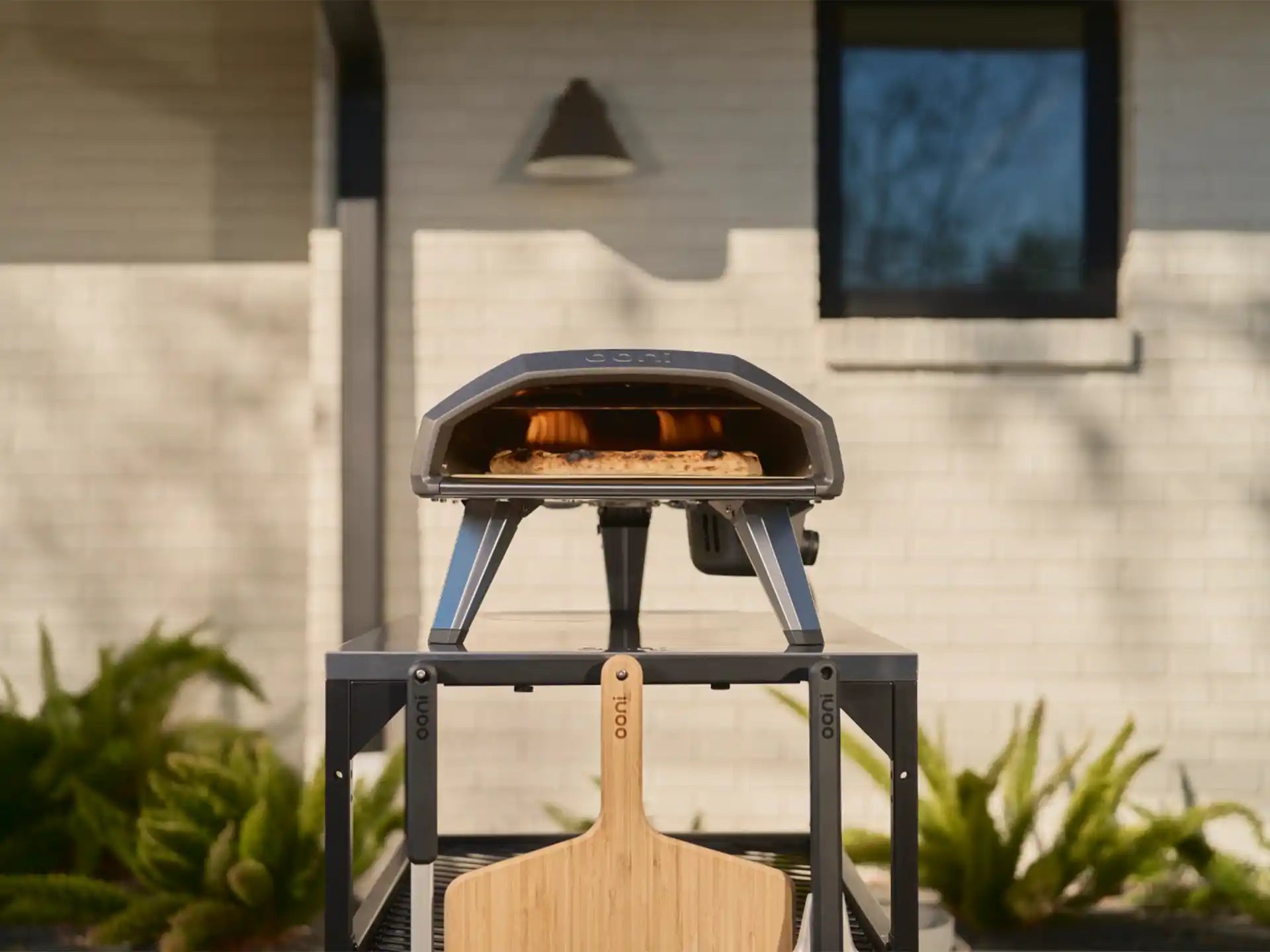 Ooni Koda 2 gasgestookte pizza oven buiten op tafel, geplaatst in de tuin tijdens gebruik.
