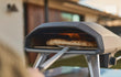 Ooni Koda 2 gas pizza oven, close-up van pizza die bakt in de oven met zichtbare vlam, sfeervolle setting.
