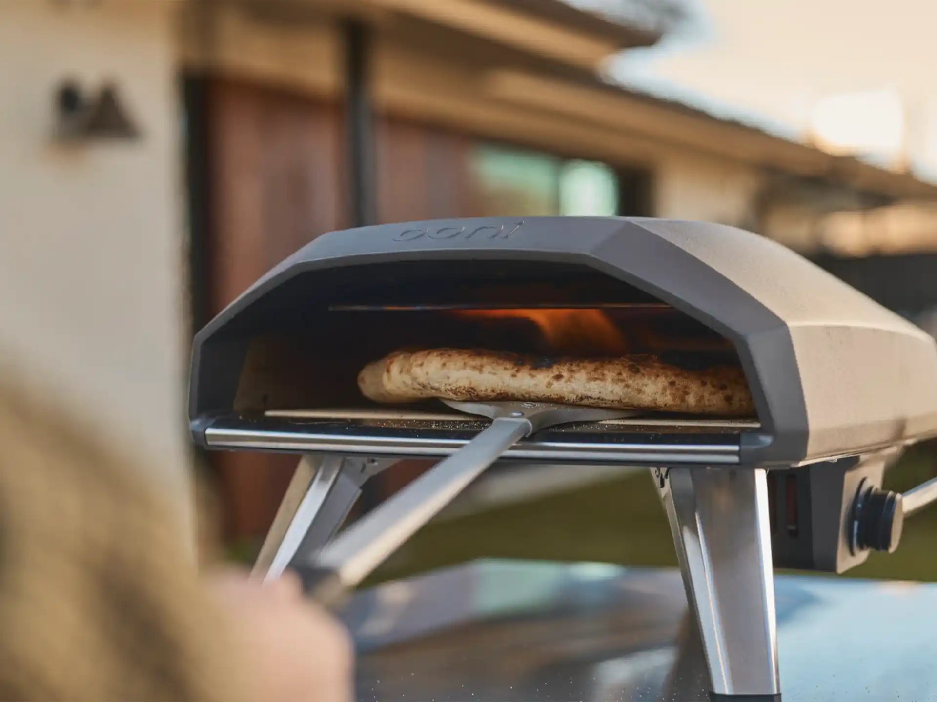 Ooni Koda 2 gas pizza oven, close-up van pizza die bakt in de oven met zichtbare vlam, sfeervolle setting.
