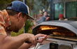 Ooni Koda 2 Pro gasgestookte pizza oven in gebruik buiten, persoon schuift pizza in de oven met pizzaschep.