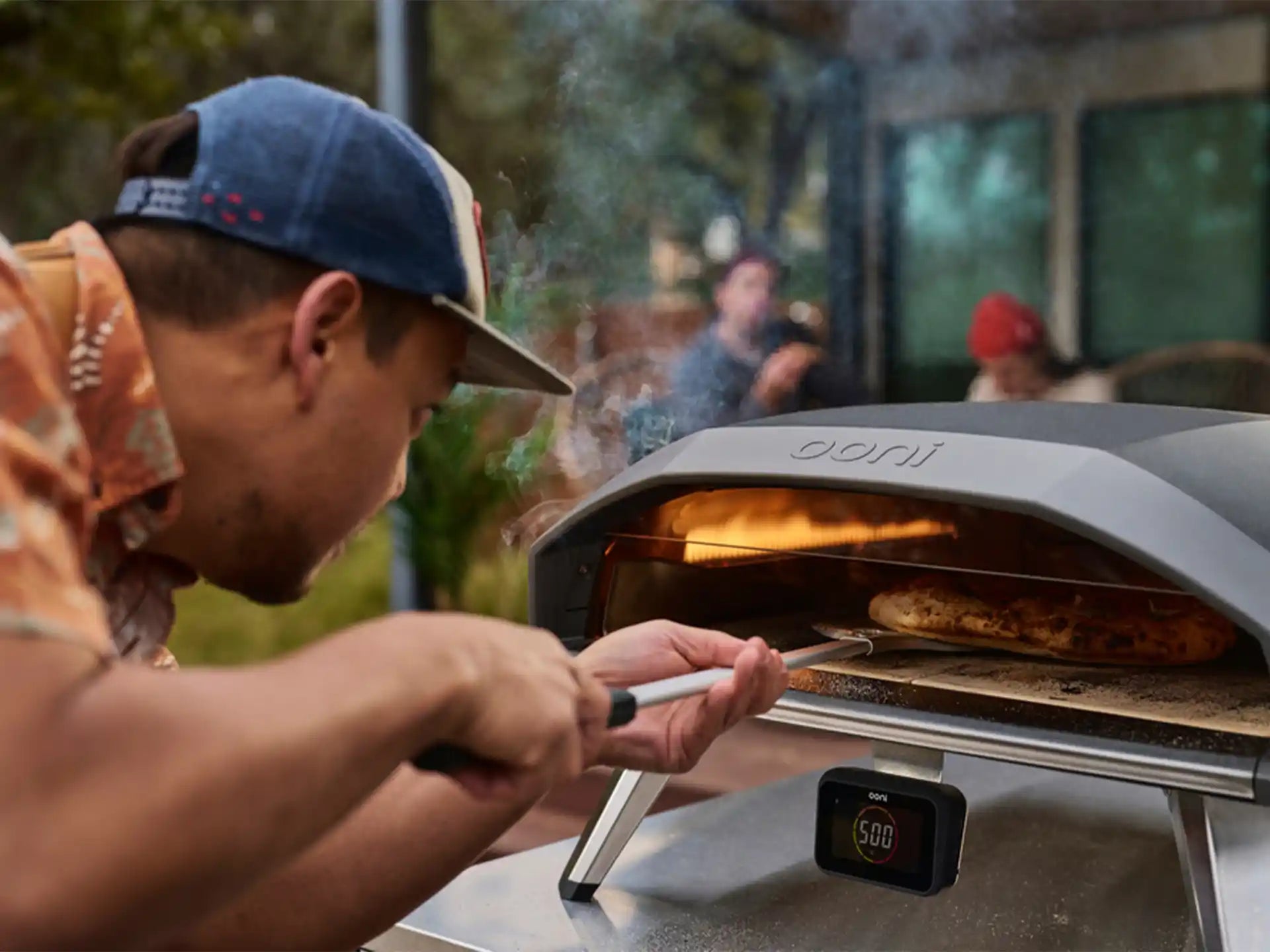 Ooni Koda 2 Pro gasgestookte pizza oven in gebruik buiten, persoon schuift pizza in de oven met pizzaschep.