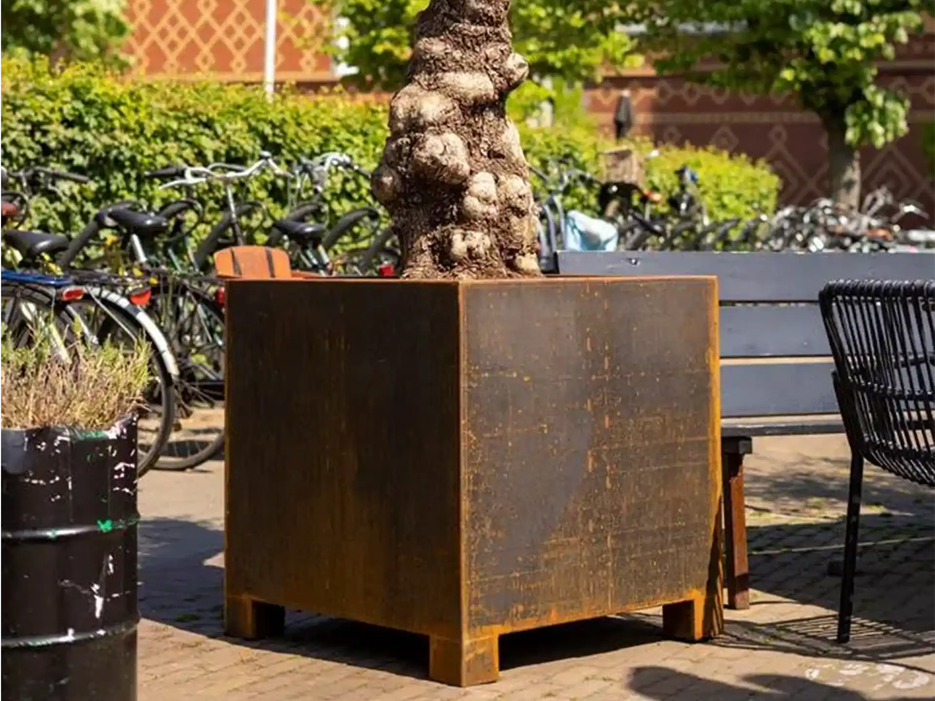 Vierkante Adezz Carrez Cortenstaal Plantenbak Rechthoek met poten en bodem, beplant en geplaatst naast een zithoek.
