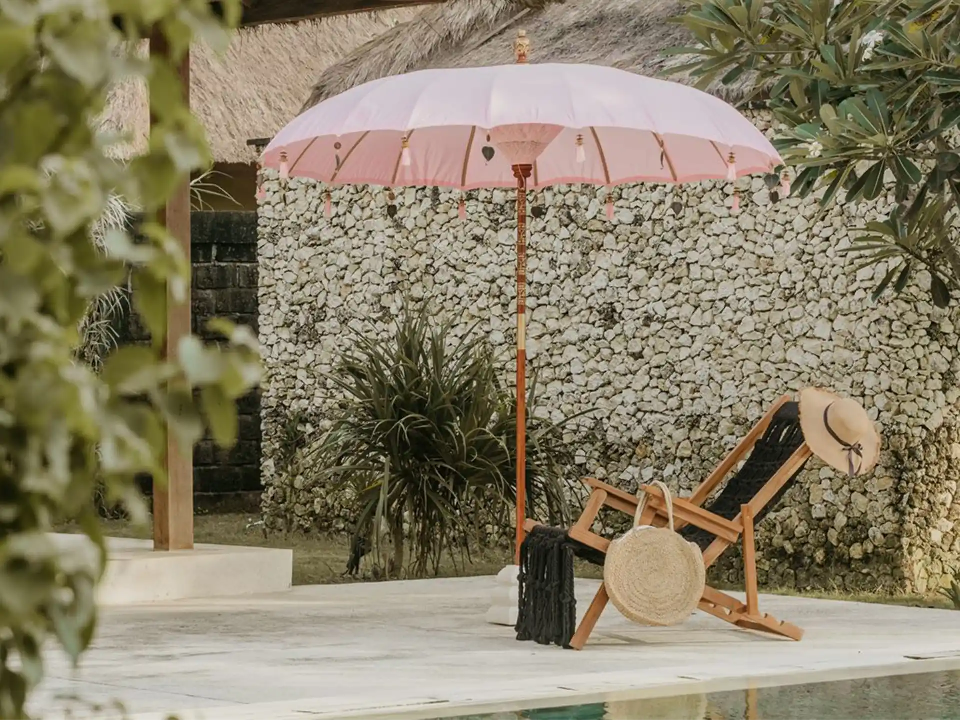 Roze Bali parasol van Todo Bien naast ligstoel bij zwembad, zorgt voor een tropische en sfeervolle tuinsetting.