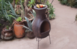 Sfeerfoto van de bruine Sol-y-Yo Barbecue terrashaard Acapulco (ø46 x 100 cm), brandend met open vuur en gebruikt als barbecue in een sfeervolle tuinomgeving.