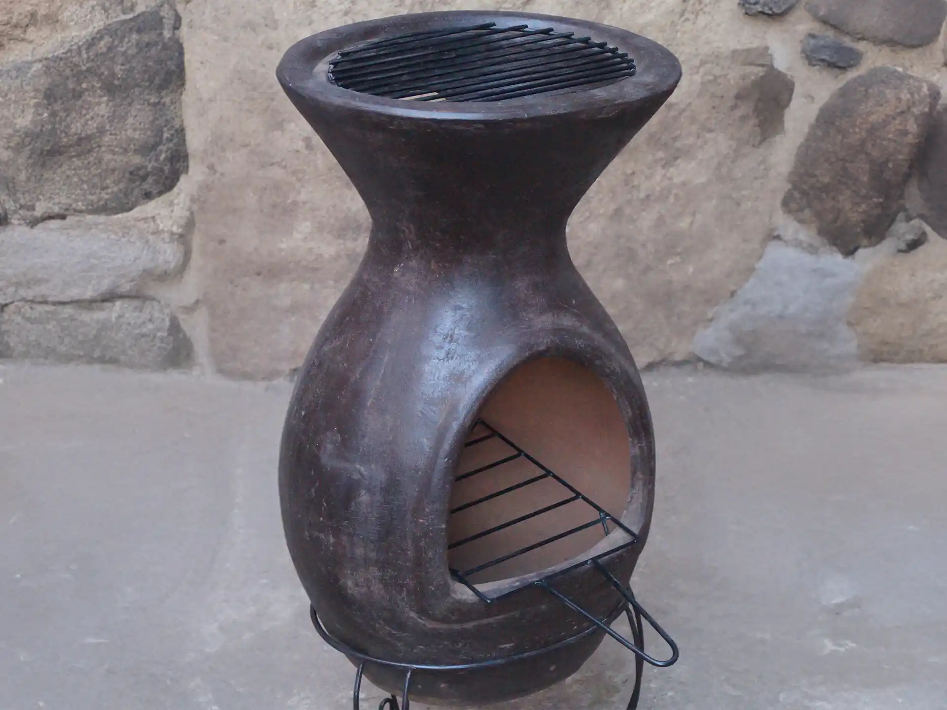 Sfeerfoto van het Sol-y-Yo Chimenea grillrooster, geplaatst op de Mexicaanse terrashaard / BBQ (46 x 106 cm), gebruikt voor het bereiden van gerechten boven brandend vuur in een sfeervolle tuinomgeving.