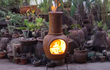 Sfeerfoto van de gele Sol-y-Yo Chimenea Mexicaanse terracotta kachel (105 cm) brandend met houtvuur in de tuin voor warmte en gezelligheid.
