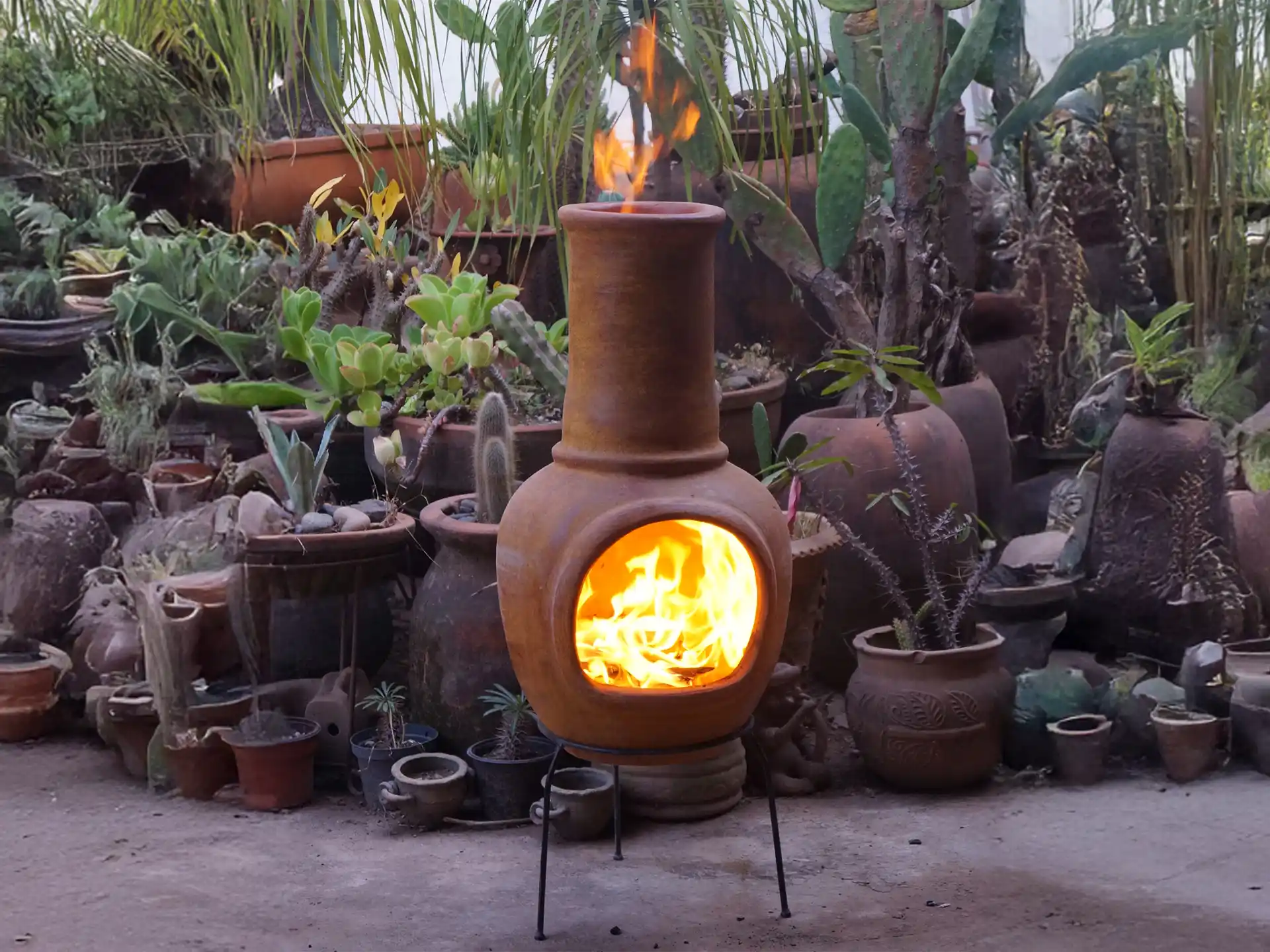 Sfeerfoto van de gele Sol-y-Yo Chimenea Mexicaanse terracotta kachel (105 cm) brandend met houtvuur in de tuin voor warmte en gezelligheid.