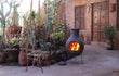 Sfeerfoto van de grijze Sol-y-Yo chimenea Mexicaanse tuinhaard Jumbo (115 cm), brandend met open vuur in een sfeervolle tuinomgeving voor warmte en gezelligheid.