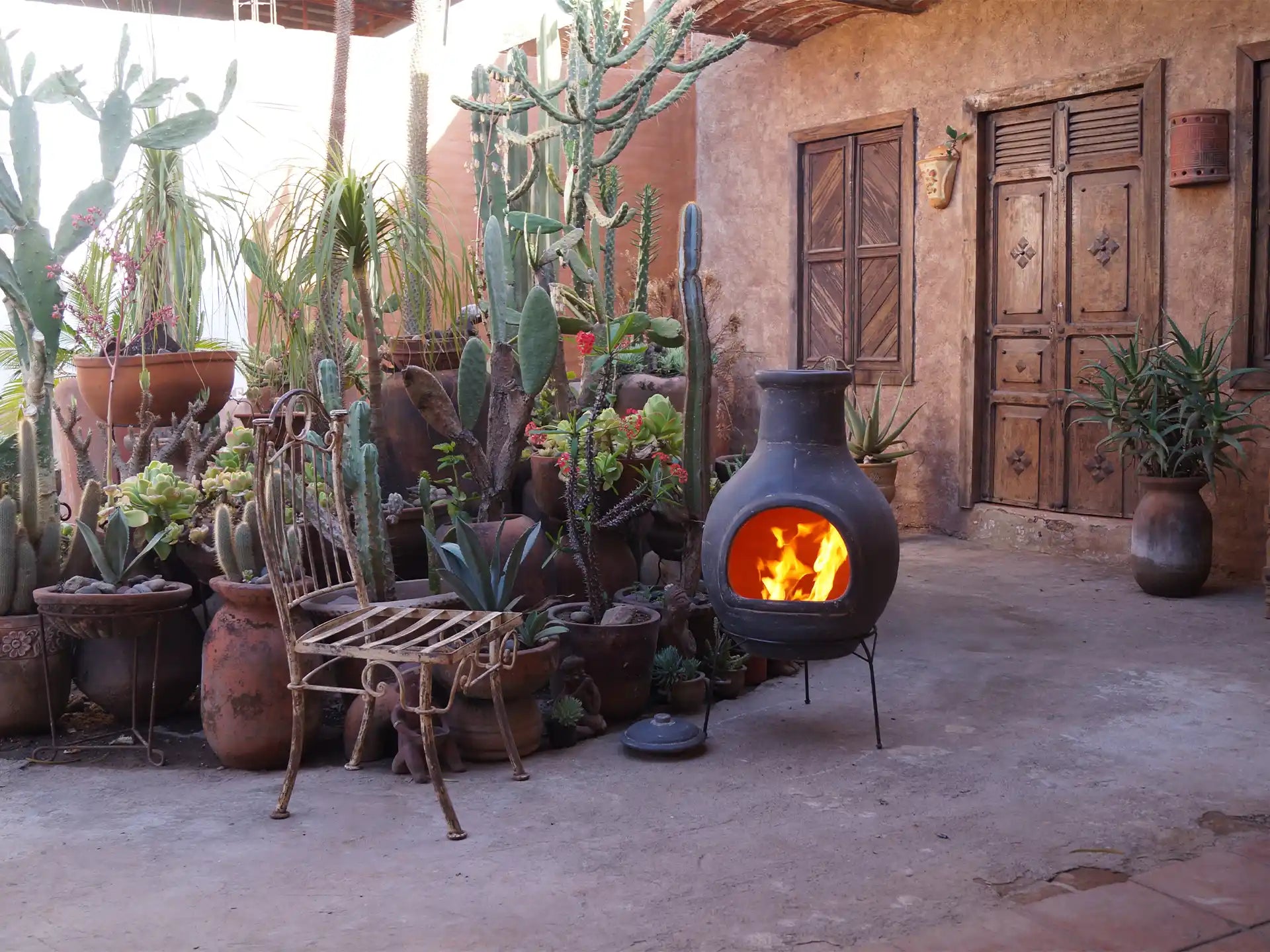 Sfeerfoto van de grijze Sol-y-Yo chimenea Mexicaanse tuinhaard Jumbo (115 cm), brandend met open vuur in een sfeervolle tuinomgeving voor warmte en gezelligheid.